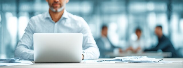 Close-up of businessman at desk with charts and laptop, blurred colleagues in background, representing corporate teamwork and data analysis.