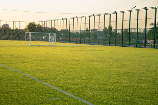 Green artificial soccer field in late afternoon with goalposts and fencing. English football pitch
