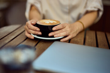 Woman Holding Coffee Cup At Outdoor Table With Laptop In Cozy Cafe Setting