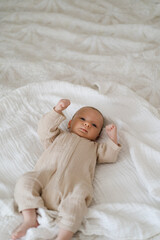 Cute baby lying on a soft white blanket with a calm expression while raising arms. Beautiful...