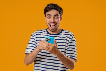 Shocked young Slavic man staring at smartphone on yellow studio with open mouth