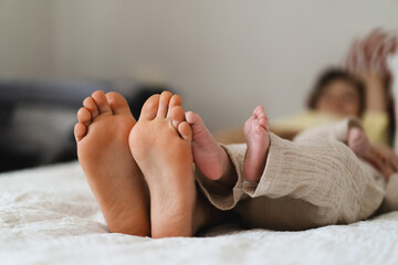 Two pairs of feet two little boys brothers rest on a soft, white bedspread, symbolizing connection and joy in family life. Moments of relaxation are shared between family members at home.