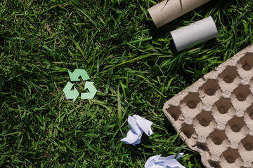 concept of ecology and recycling waste - paper, glass, plastic, cardboard, green grass in the background. Recycling eco symbol, reuse, conscious consumption, caring for nature flat lay, top view