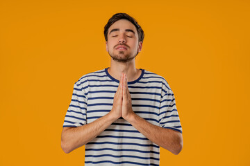 Young man praying with palms on yellow background. Guy begs satisfy desires