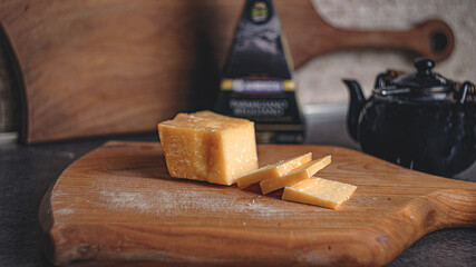 Sliced parmesan cheese on a thick cherry wood board. In the background a walnut cutting board and a...