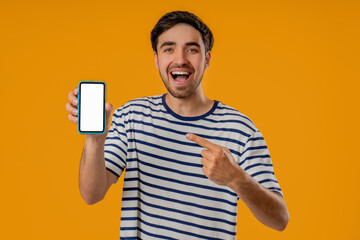 Surprised young Slavic man pointing at smartphone screen on yellow background