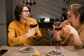 couple having romantic dinner in authentic kitchen at home, sitting at table drinking red wine. Celebrating birthday at home