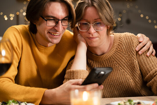 Couple during dinner looking social media at a smartphone in kitchen. - Powered by Adobe