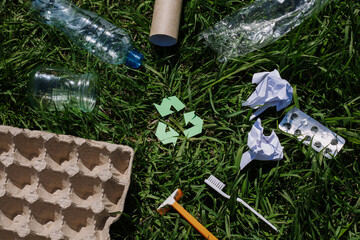 concept of ecology and recycling waste - paper, glass, plastic, cardboard, green grass in the background. Recycling eco symbol, reuse, conscious consumption, caring for nature flat lay, top view