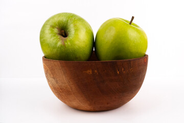 Two crisp green apples rest inside a small dark wooden bowl for snack time.