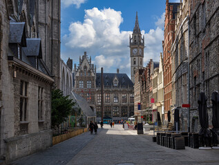 Old narrow street with tables of cafe in Ghent (Gent) and Gent Town Hall, Belgium. Architecture and landmark of Ghent. Cozy cityscape of Ghent.