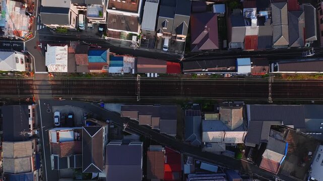Aerial view of Osaka, Japan, showing rooftops, narrow streets, and a railway with active train movement during golden hour lighting.