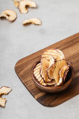 Apple chips in a wooden bowl on a light gray background.
