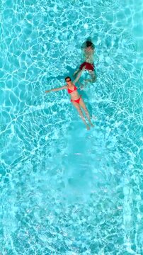 Top down view as a man dives into the pool while woman is laying on her back