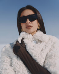 A beautiful and stylish girl in a fur coat walks on a sunny winter day on the frozen sea