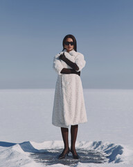 A beautiful and stylish girl in a fur coat walks on a sunny winter day on the frozen sea