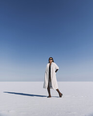 A beautiful and stylish girl in a fur coat walks on a sunny winter day on the frozen sea