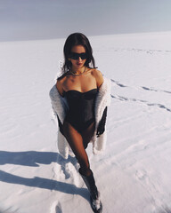 A beautiful and stylish girl in a fur coat walks on a sunny winter day on the frozen sea