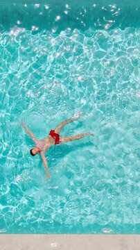 Top down view of a man in red shorts swims on his back in the pool.