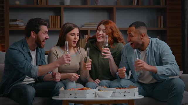 Happy multiracial four friends screaming rejoicing watching TV group diverse people fans men women watch television sport at home party celebrating clinking bottles drinking beer cheers enjoy victory
