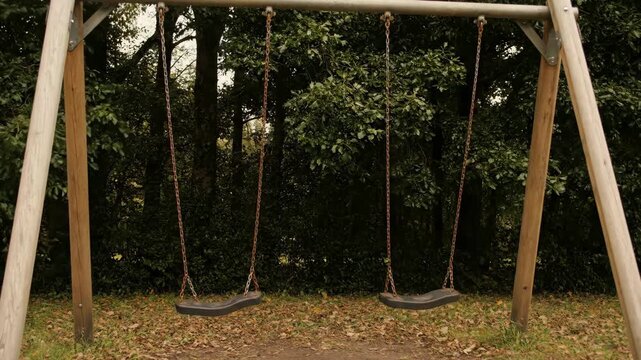 Empty swing set moving gently in the breeze at a quiet park, symbolic Labor Day holiday concept, no people.
