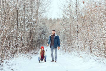 Dad pulling sled with his daughter on it in a winter forest