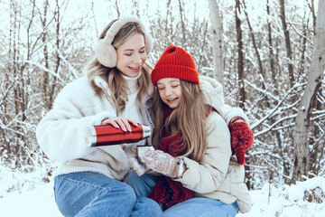 Obraz premium Cute young mom pouring tea from thermos and giving to a kid