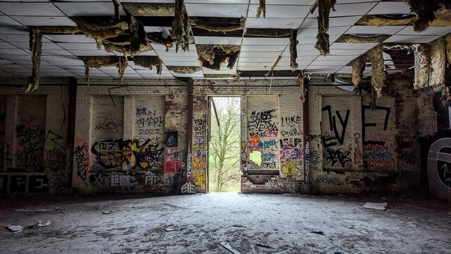 Abandoned industrial factory warehouse building interior. Dark empty Rishton Paper Mill. Broken ceiling tiles, dusty floor, graffiti walls. Daylight though open doorway, escape urban decay to nature. - Powered by Adobe