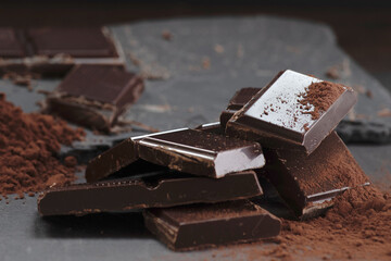 Broken dark chocolate and cocoa powder on a dark table