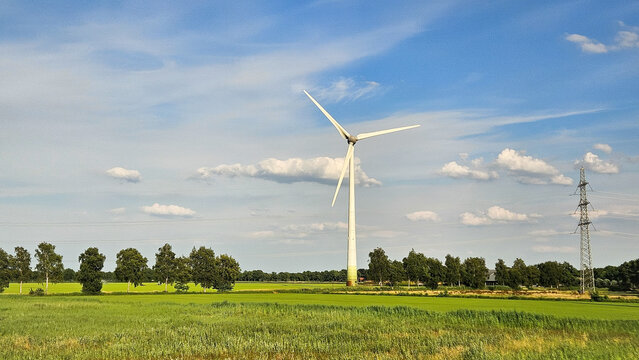 Wind turbine in landscape with line of trees. Dutch nature scene with green energy generator.