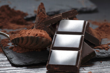 Broken dark chocolate and cocoa powder on a dark table