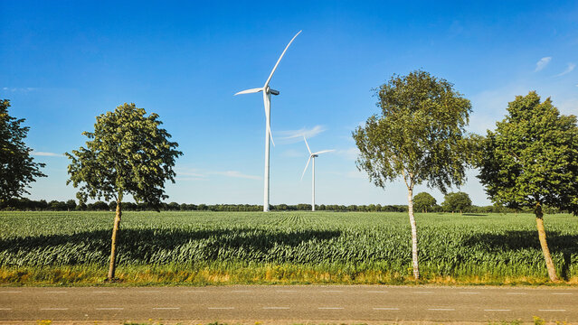 Landscape photo of two tall thite wind turbines in meadow farming field. Rnewable energy, global warming, climate change, sustainability, farm land concept.  - Powered by Adobe