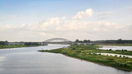 Fototapeta premium Bridge crossing river in nature landscape. Dutch IJsselbrug over IJssel river near European city.