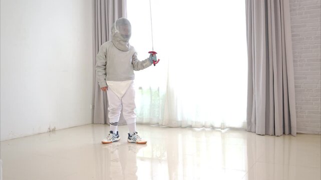 Before the tournament day, a boy dressed in fencing gear are rehearsing in gym