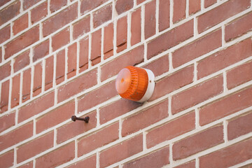 Orange alarm warning light mounted on brick wall, modern security and monitoring system. Surveillance technology for safety and protection on house in neighborhood. Danger warning alert equipment.