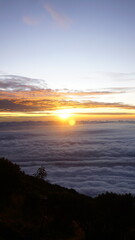 Obraz premium Breathtaking sunrise viewed from a mountaintop, with the sun glowing over a vast sea of clouds.