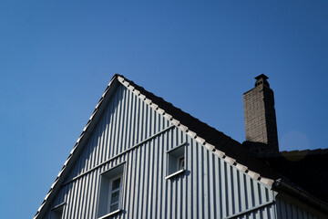 Upper part of a blue house with pointed roof, windows and chimney, against a clear blue sky.
