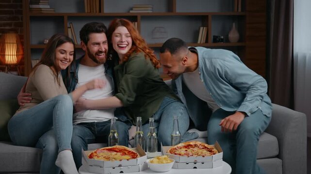 Caucasian man sit at home party waiting guests multiracial friends coming greeting laughing smiling cuddling together four people meeting women men on couch reunion hangout clinking bottles drinking