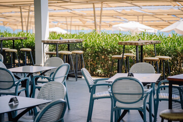 Outdoor terrace with modern tables, chairs, and bar stools under large sunshades. A stylish empty seating area in a sunny resort or beachside café.
