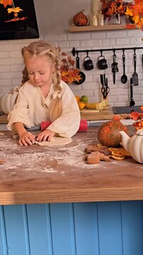 A little girl using cookie cutters to shape dough on a flour-dusted kitchen counter, surrounded by fall-themed decorations and fresh pumpkins. Halloween.  Autumn concept,  autumn season,  fall