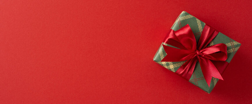 Wrapped banner gift box with a red ribbon rests on a bold red backdrop, conveying holiday magic, generosity, celebration, warmth, and festive charm suited for Christmas and New Year greetings