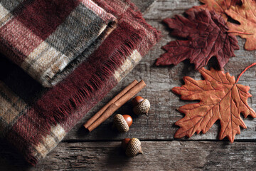  Cozy autumnal arrangement featuring a folded wool blanket with plaid pattern, cinnamon sticks, acorns, and faux maple leaves