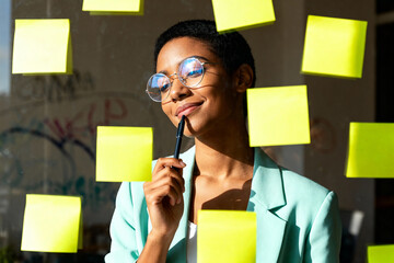 Creative businesswoman brainstorming ideas with sticky notes on window