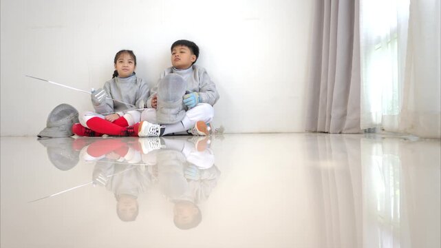 Before the tournament day, a boy and girl dressed in fencing gear are rehearsing in gym