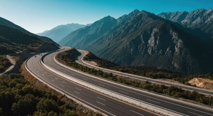 Winding highway cuts through mountain landscape.  A high-angle view of a multi-lane highway snaking through a valley, surrounded by lush greenery and majestic mountains