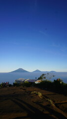 Naklejka premium Panoramic view of a mountain landscape at sunrise, with a sea of clouds filling the valley below and a clear blue sky above.