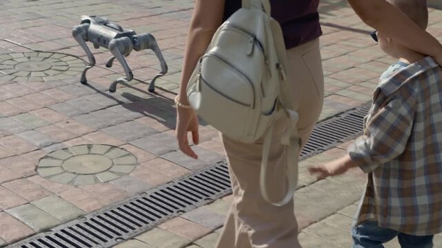 Woman and her young son walking down a city street with a futuristic four-legged robot companion