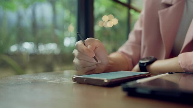 Asian professional woman multitasking with smartwatch and stylus on tablet, concept of digital career and time management