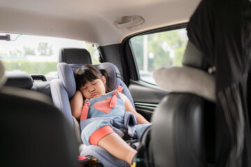 A cute little Asian girl is sleeping in a child car seat inside a car during a travel trip,A cute little Asian girl is sleeping in her car seat while hugging a doll.