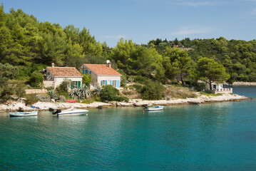 Obraz premium Naturstein-Häuser mit terrakotta-farbenem Ziegeldach, Boote und Kiefernwald an der felsigen Küste mit türkisfarbenem Meer auf der Insel Losinj, Kroatien
